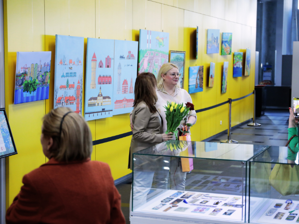 osoby na wernisażu pod ścianą z obrazami